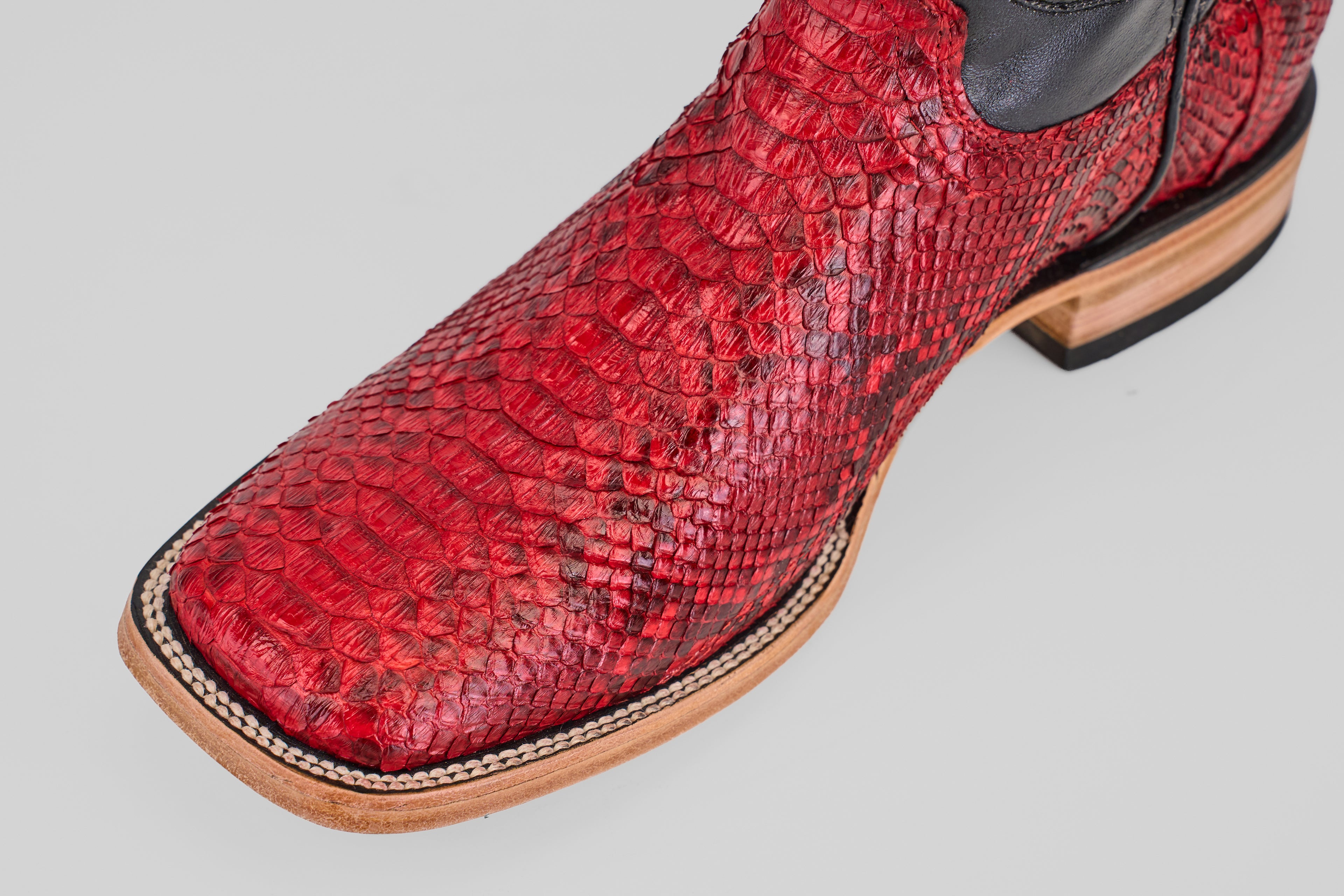 A close-up of the Tanner - Ruby - Square Toe cowboy boot, showcasing its Python Rojo snakeskin, square toe design, and detailed stitching on a light background.