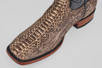 A close-up of the Tanner - Rustic Bone - Square Toe boot highlights its brown python design, black trim, and wooden sole, showcasing Western craftsmanship against a light gray background.