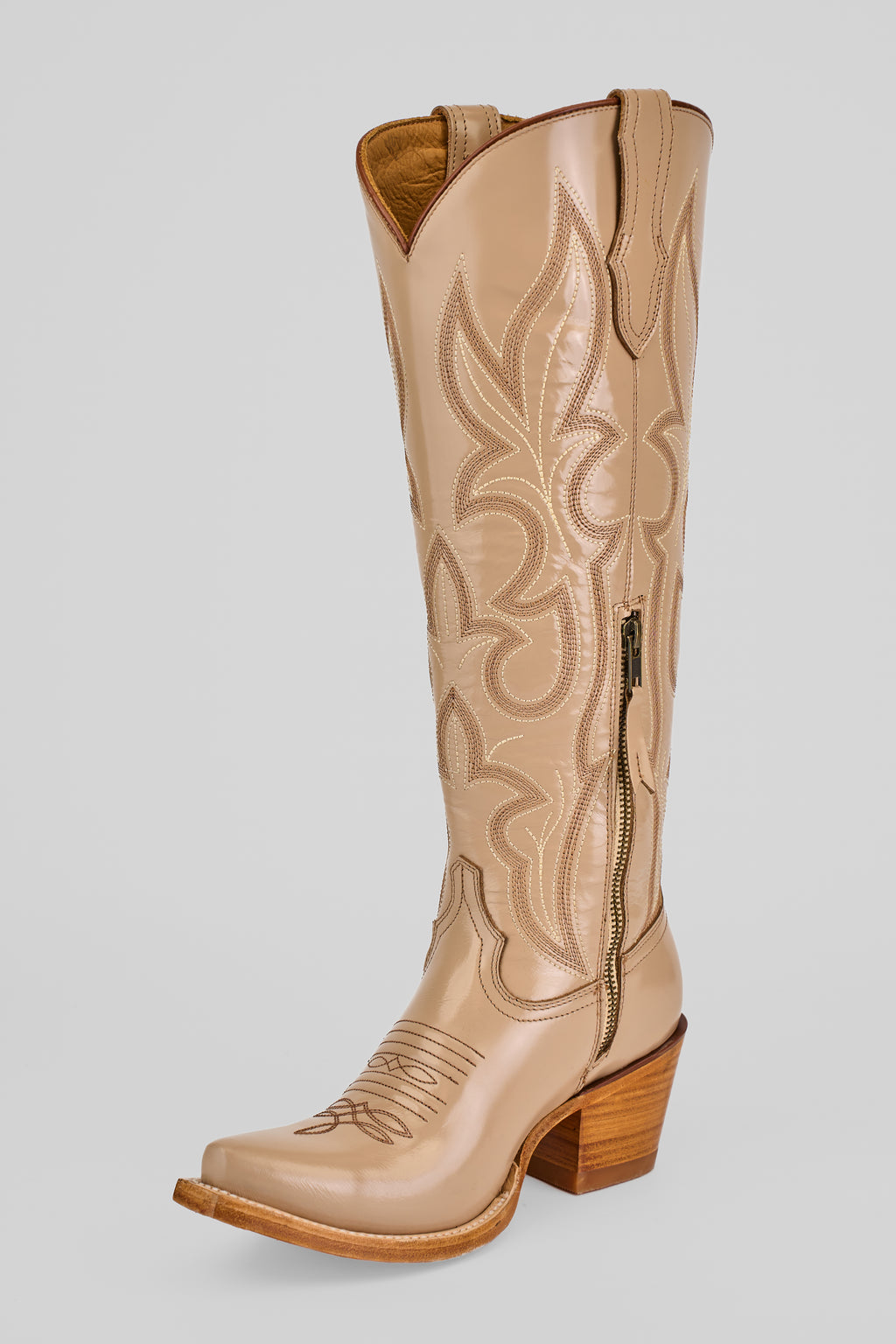 The Allison Cream Tall Shaft Snip Toe women’s boot, featuring decorative stitching, a side zipper, and a stacked wooden heel, is shown in tan on a plain light background.