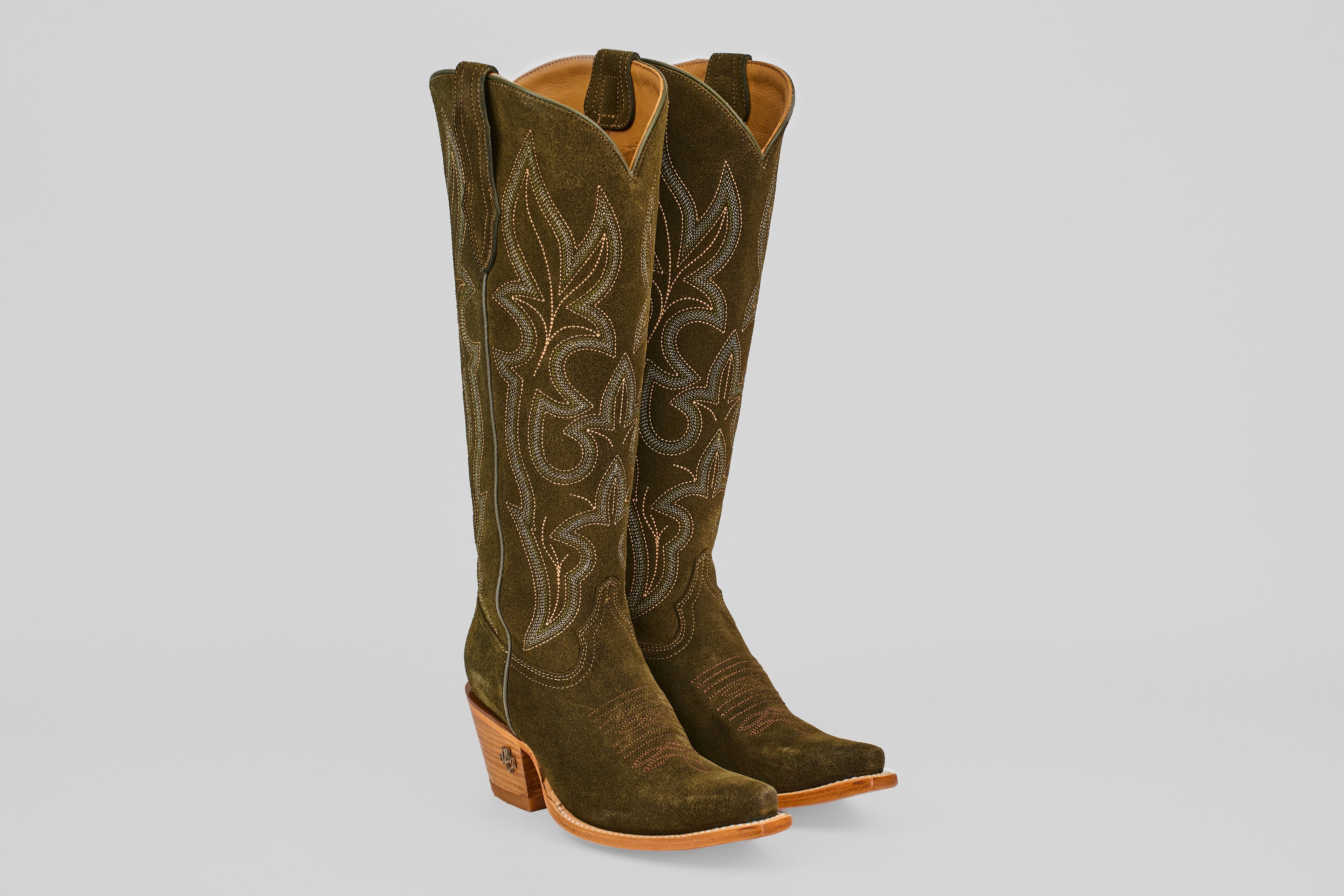 A pair of Allison Agave - Tall Shaft - Snip Toe women’s cowboy boots in dark green suede with tan stitching, pointed toes, and light brown stacked heels are standing upright against a light gray background.