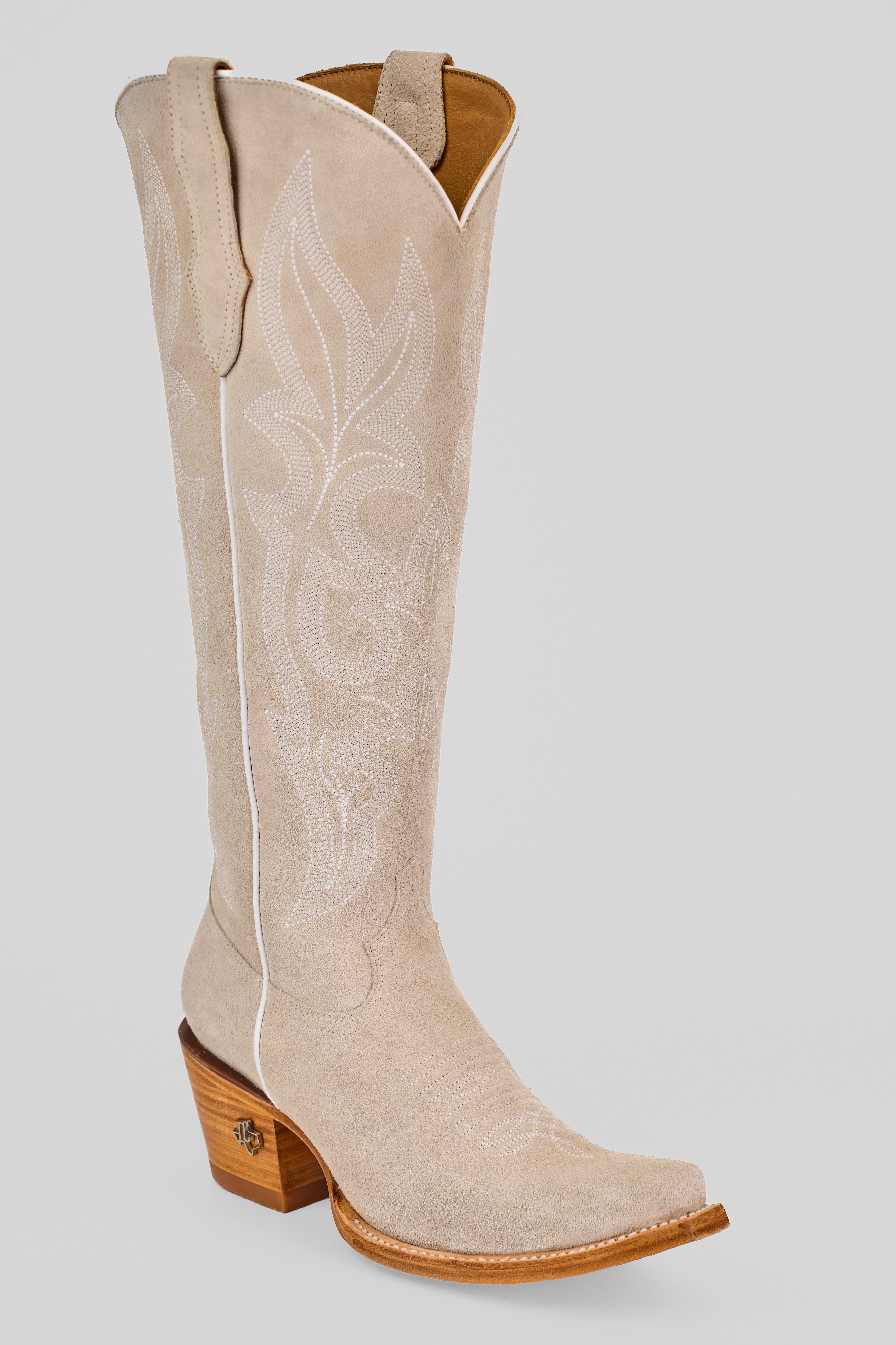 The Allison Ivory - Tall Shaft - Snip Toe boot features light beige suede, decorative white stitching, a pointed toe, wooden angled heel, and pull straps, shown against a plain light gray background.