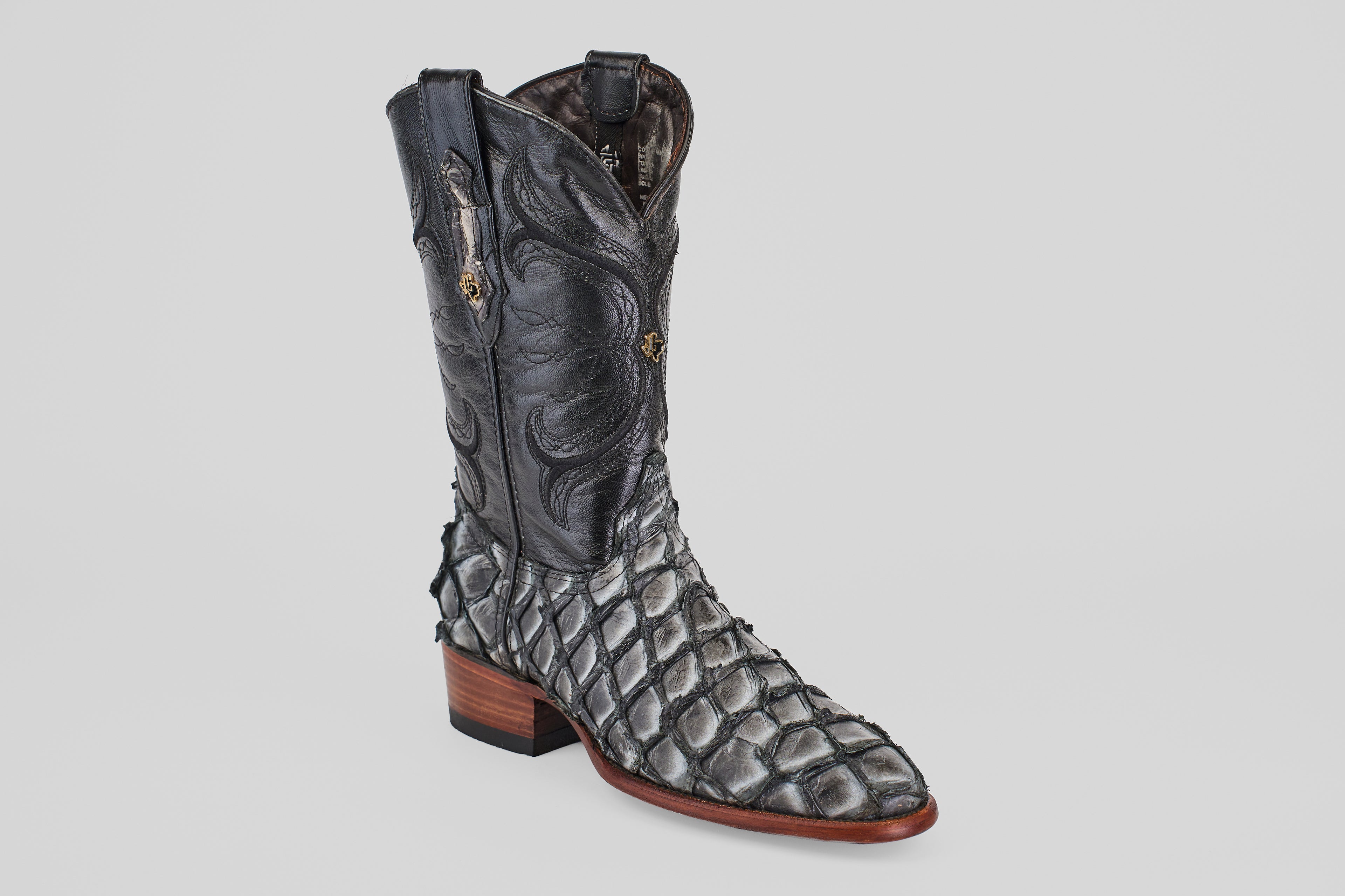 The Conor - Newspaper - Roper Toe is a unique boot with a black stitched upper, scaly pirarucu-style lower, and brown stacked heel—ideal for those seeking standout exotic roper toe boots.