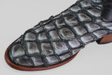 Close-up of the Conor - Newspaper - Roper Toe boot, crafted from black and grey reptile skin with a striking scale pattern and a wooden sole, displayed against a plain light background.