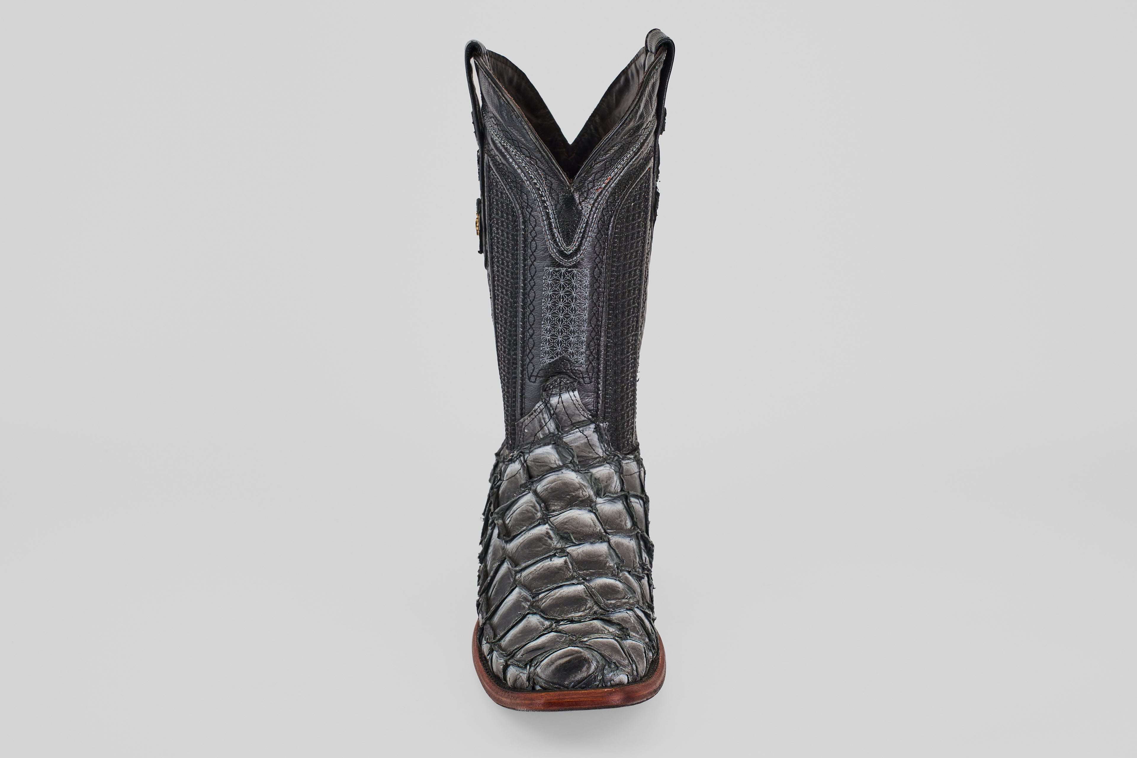 The Conor - Newspaper boot features a black, narrow square toe with a reptile-textured foot, decorative shaft stitching, and a brown sole, shown facing forward against a plain light background.
