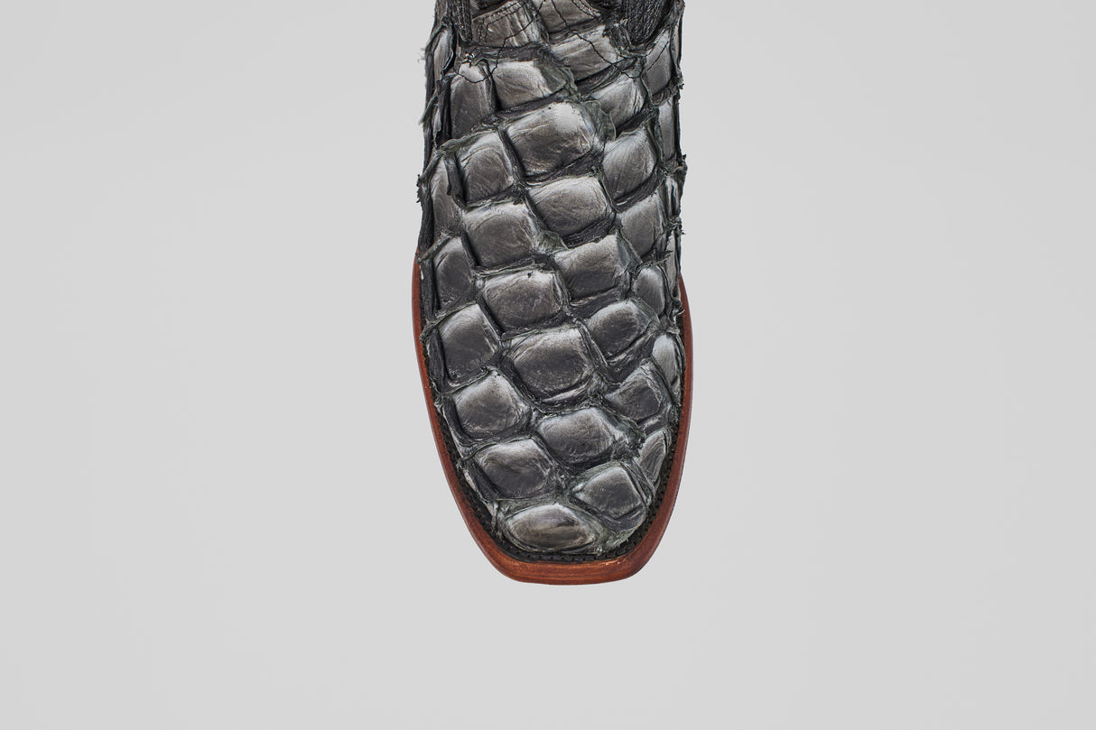 Close-up of the Conor - Newspaper cowboy boot toe in black fish leather with a narrow square toe and brown sole, set against a plain white background.