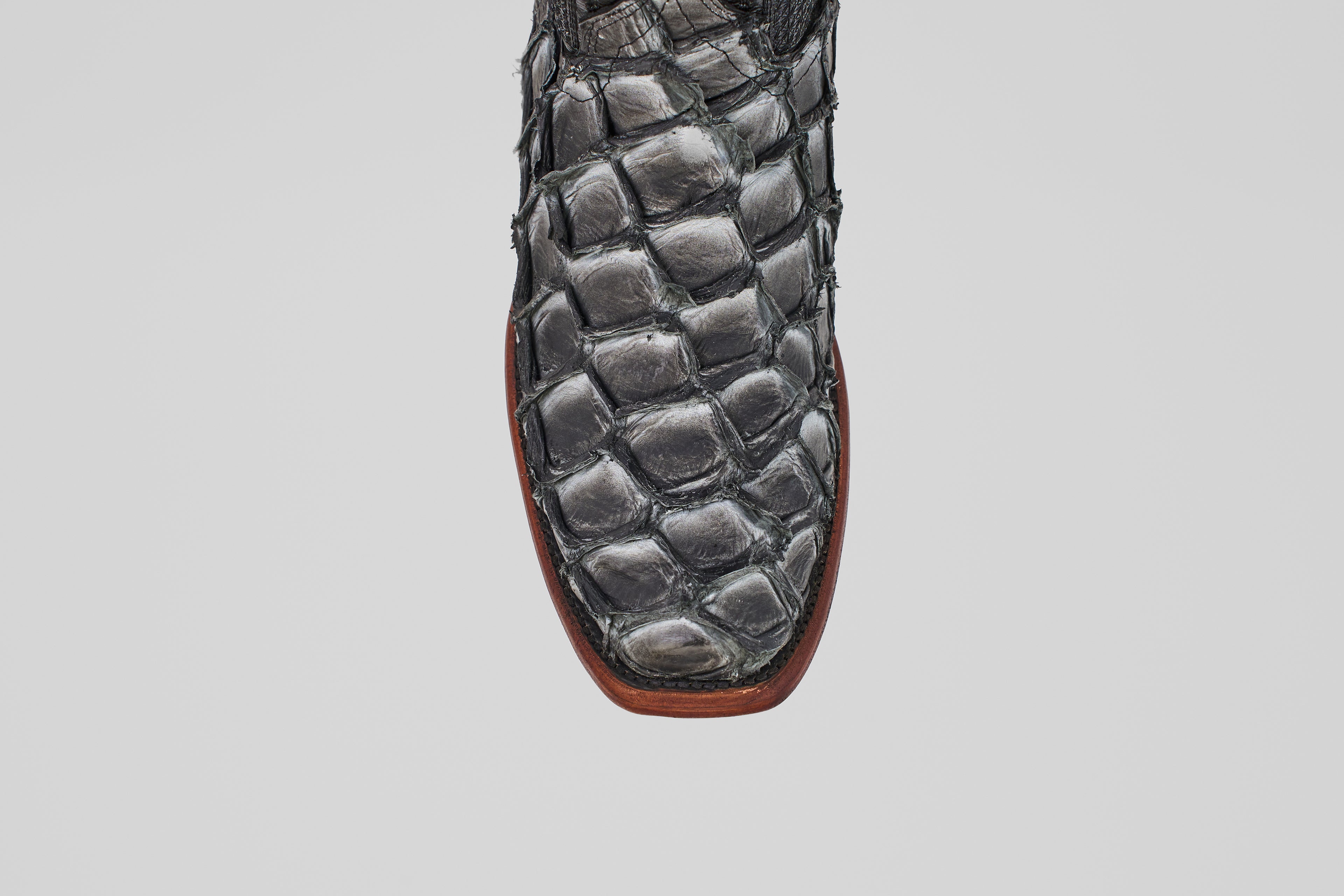 Close-up of the Conor - Newspaper cowboy boot toe in black fish leather with a narrow square toe and brown sole, set against a plain white background.