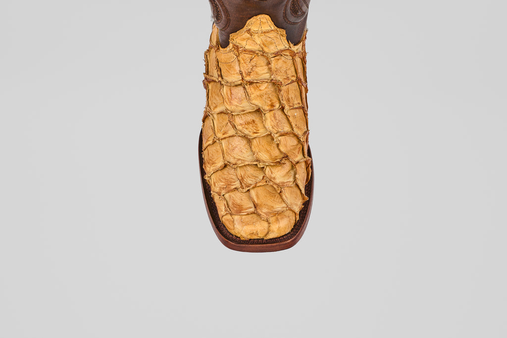 A top view of the Conor - Buttercup - Rodeo Toe boot features textured yellowish-brown leather reminiscent of exotic skin, set against a plain gray background, emphasizing its distinctive western style.