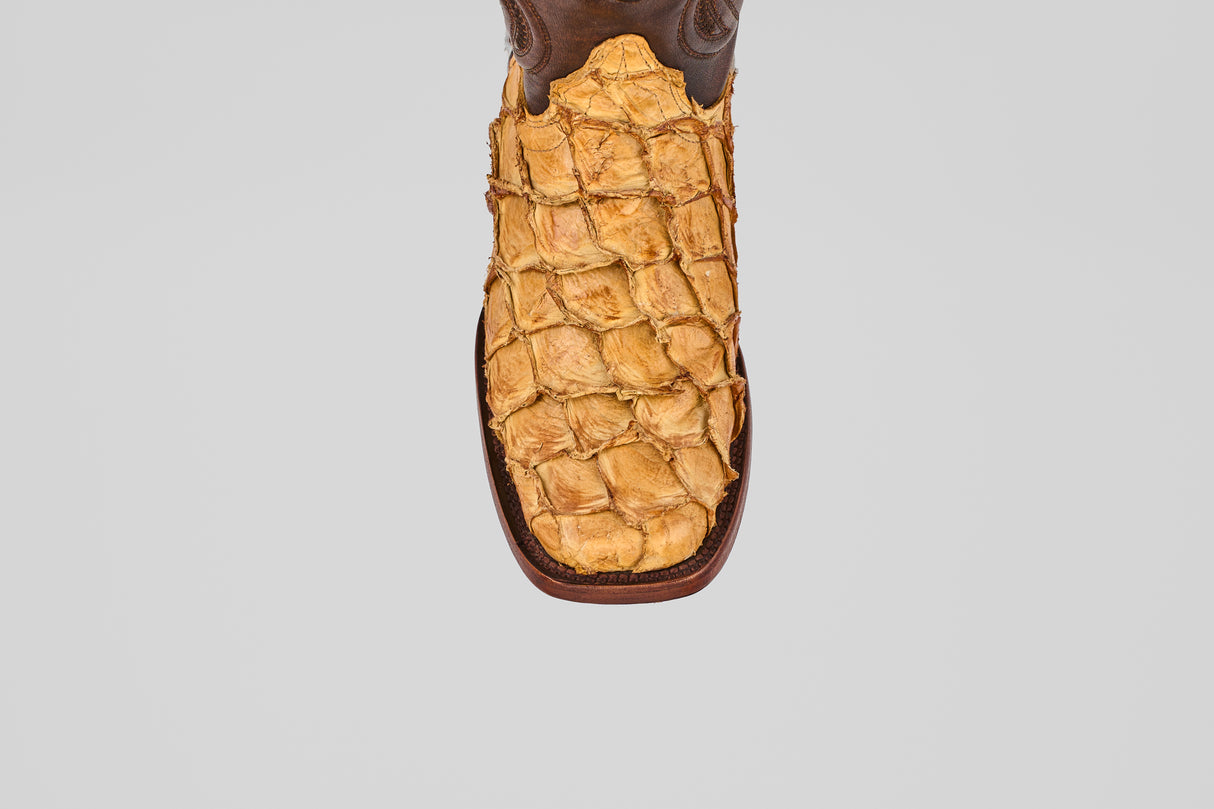 A top view of the Conor - Buttercup - Rodeo Toe boot features textured yellowish-brown leather reminiscent of exotic skin, set against a plain gray background, emphasizing its distinctive western style.