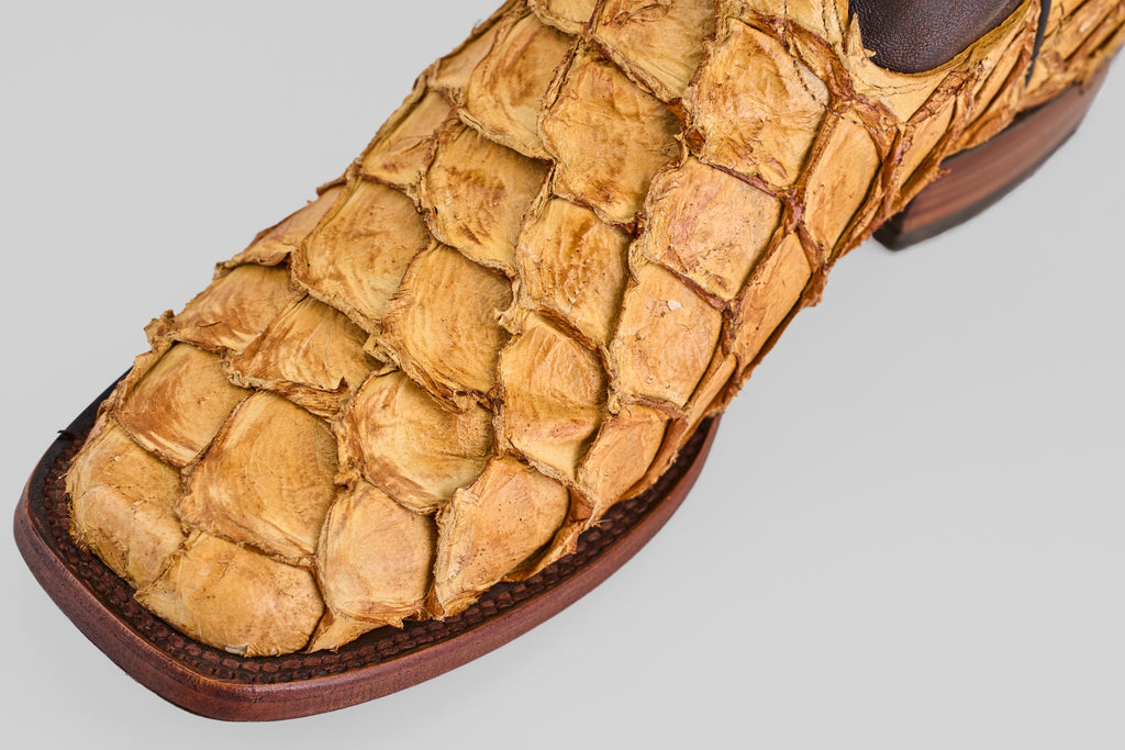 Close-up of the Conor - Buttercup - Rodeo Toe boot featuring tan fish leather with textured exotic scales, a square toe, dark brown sole, and visible stitching for western flair.