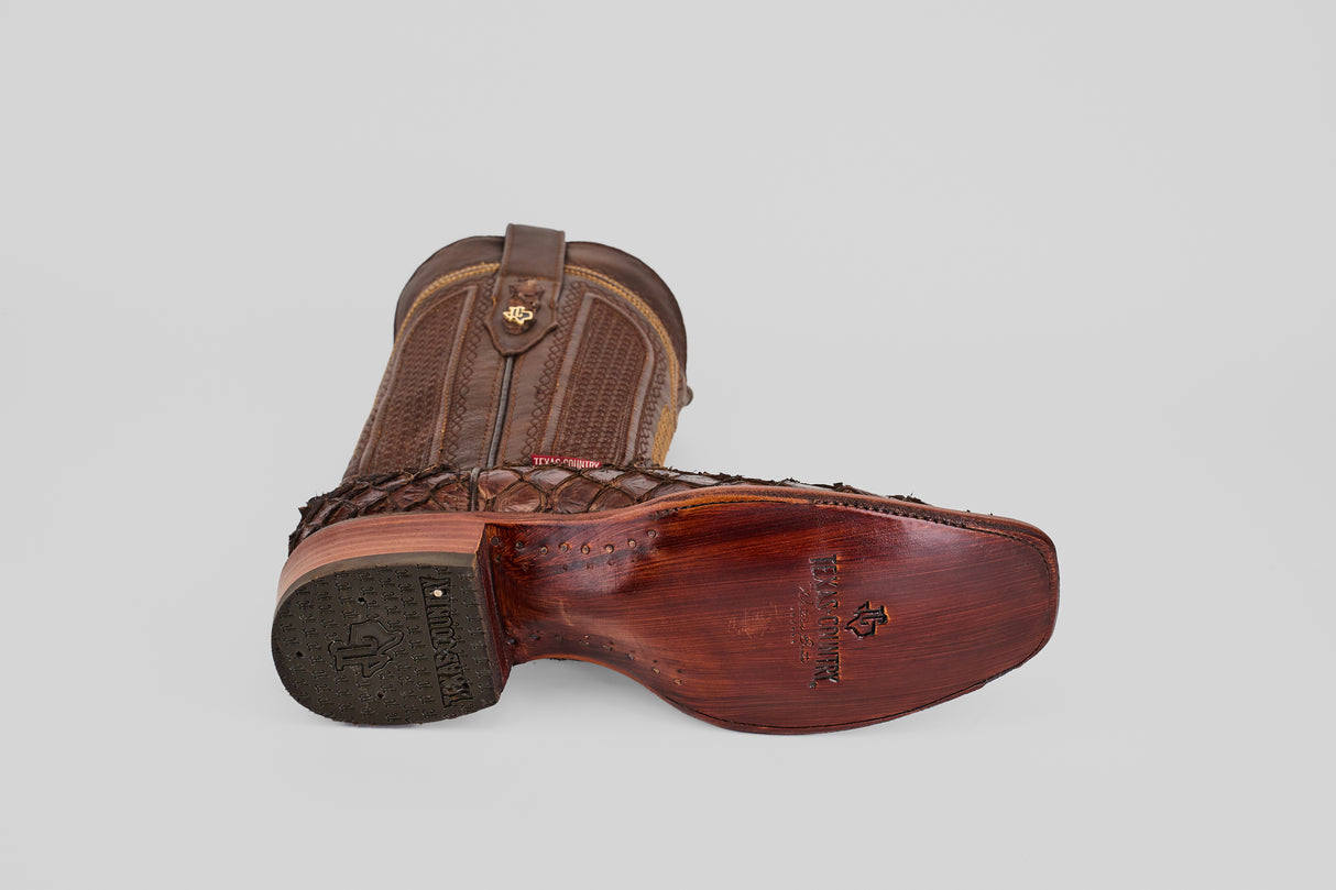 The Conor - Brown - Narrow Square Toe boots are shown, one upright and one on its side to display the textured sole and heel. Detailed stitching and embossed leather patterns add distinctive style.