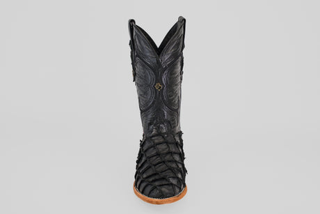 A single Conor - Matte Black - Roper Toe boot made from black pirarucu fish leather, featuring detailed stitching and textured scales on the lower section. Viewed from the front against a plain light gray background with a tan sole.