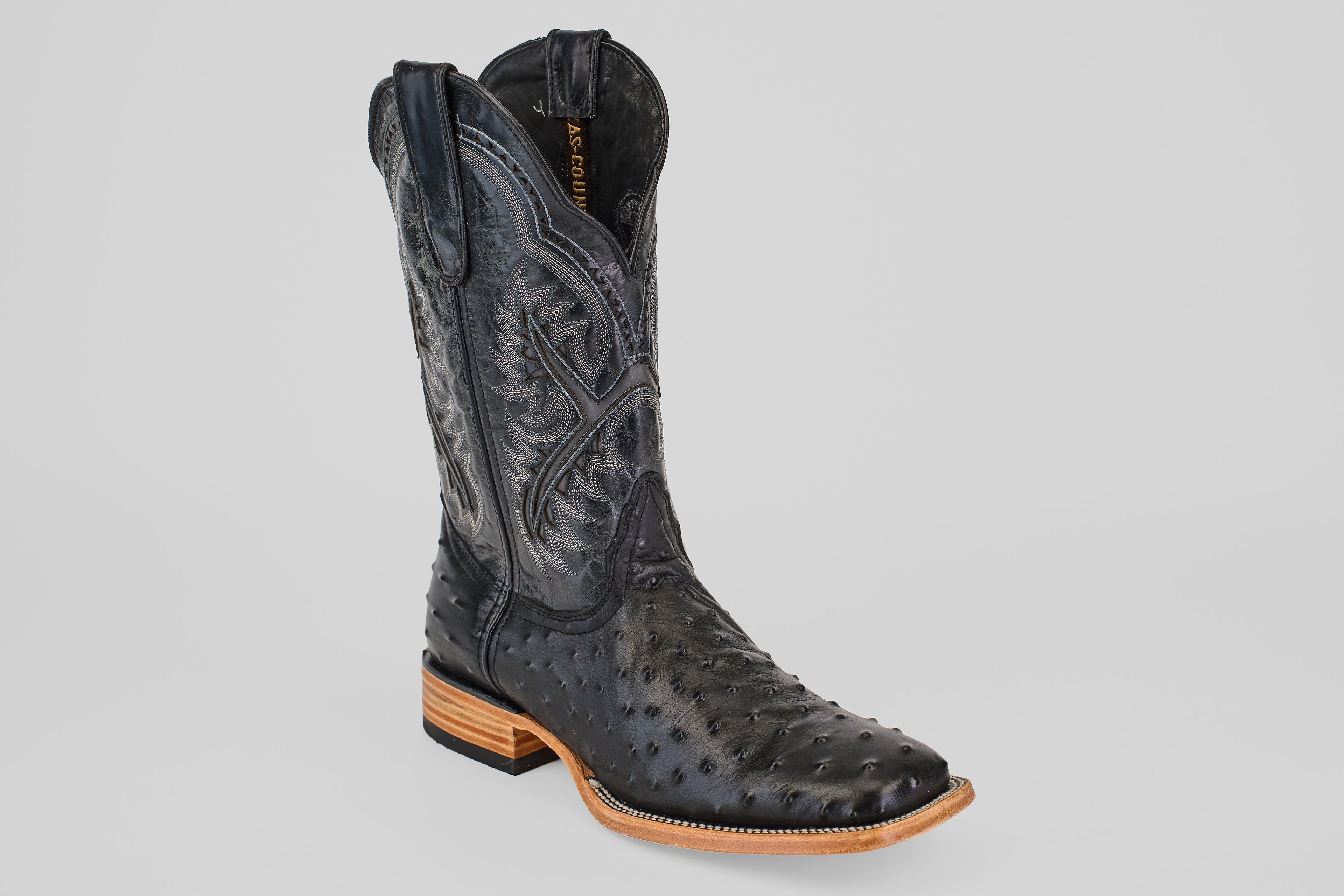 The Ostrich Black - Embossed Leather - Square Toe (E424) boot features detailed stitching, textured leather, a square toe, and a light brown stacked heel and sole, displayed on a plain light gray background.