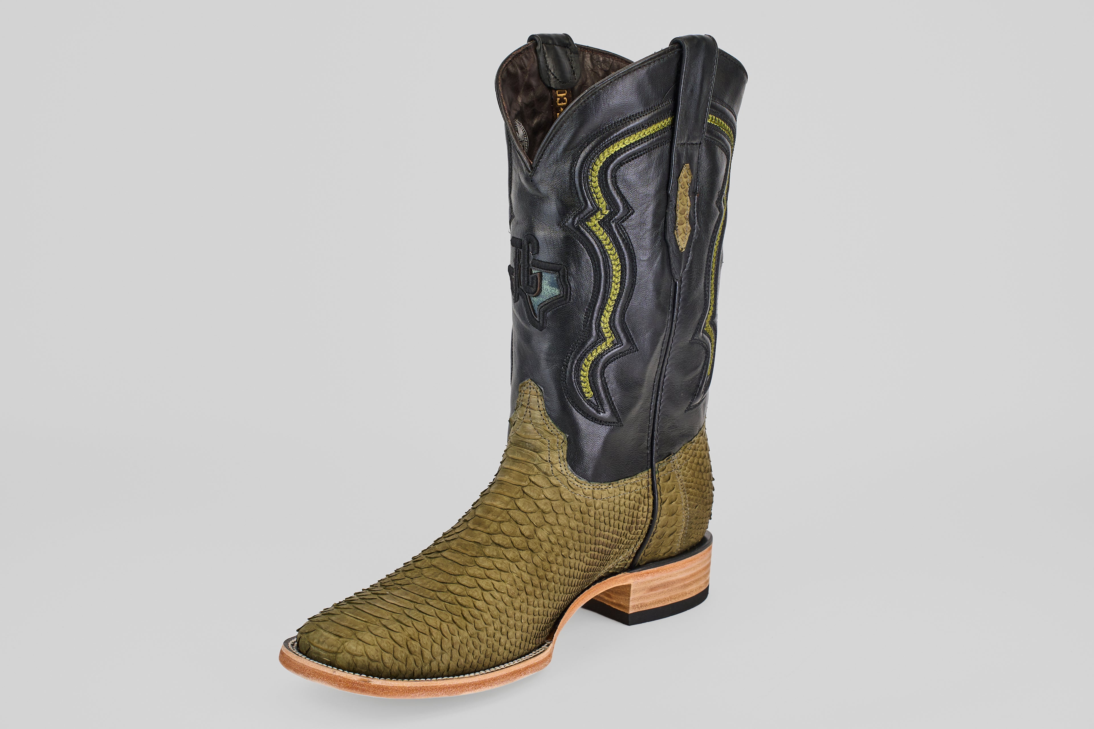 The Tanner - Green Jungle - Square Toe is a western cowboy boot with a green textured python leather lower, black leather upper with yellow and green stitching, and a wooden sole with a low heel.