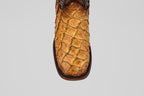 A close-up of the Conor Platinum - Buttercup - Square Toe (Herradura) cowboy boot highlights its unique pirarucu leather scale pattern and rich brown color, showcasing the premium exotic texture against a plain gray background.