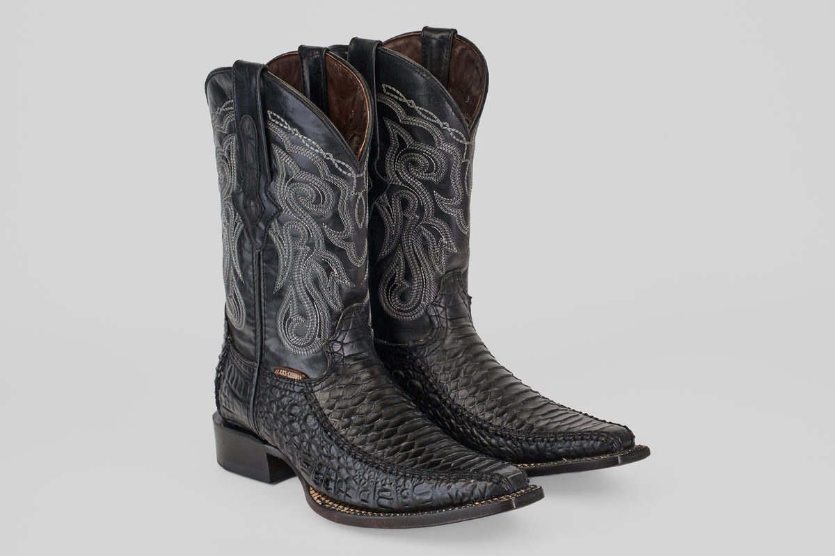 A pair of Python Black - Embossed Leather - Versy Toe (E202) cowboy boots with intricate silver stitching, pointed toes, and stacked heels is displayed on a plain light gray background.