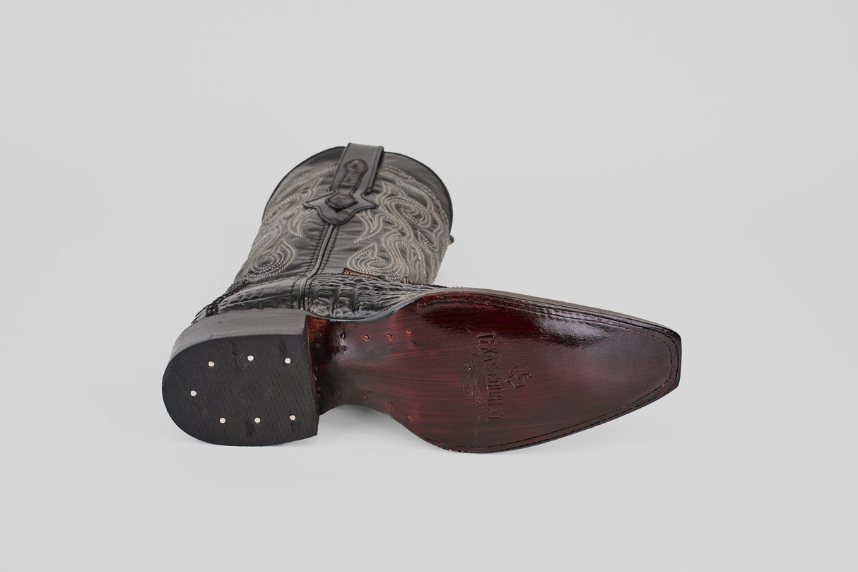 A single Python Black - Embossed Leather Versy Toe (E202) cowboy boot rests on its side, displaying the dark wooden sole with metal nails and a textured, intricately stitched upper against a light gray background.