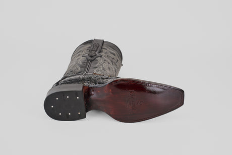 A single Python Black - Embossed Leather Versy Toe (E202) cowboy boot rests on its side, displaying the dark wooden sole with metal nails and a textured, intricately stitched upper against a light gray background.