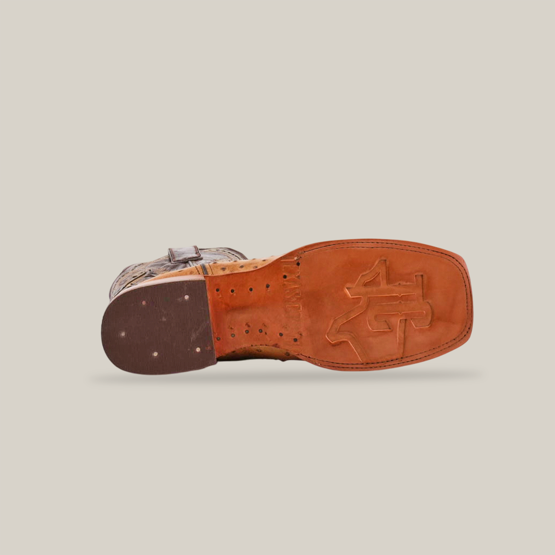 A bottom view of the Karoo Ostrich Print Orix - Square Toe boot displays a brown sole with textured treads and a prominent logo, featuring premium light tan cowhide leather in an Ostrich pattern against a plain white background.