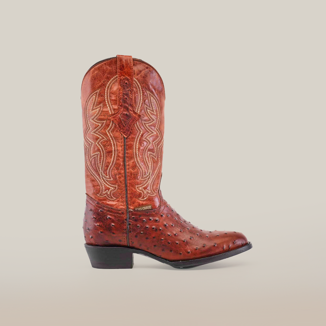 The Karoo Ostrich Print Cogñac - Round Toe is a single brown cowboy boot featuring intricate stitching and patterns. Crafted from premium materials, it has a polished, textured leather look with a pointed toe and low heel set against a plain white background.