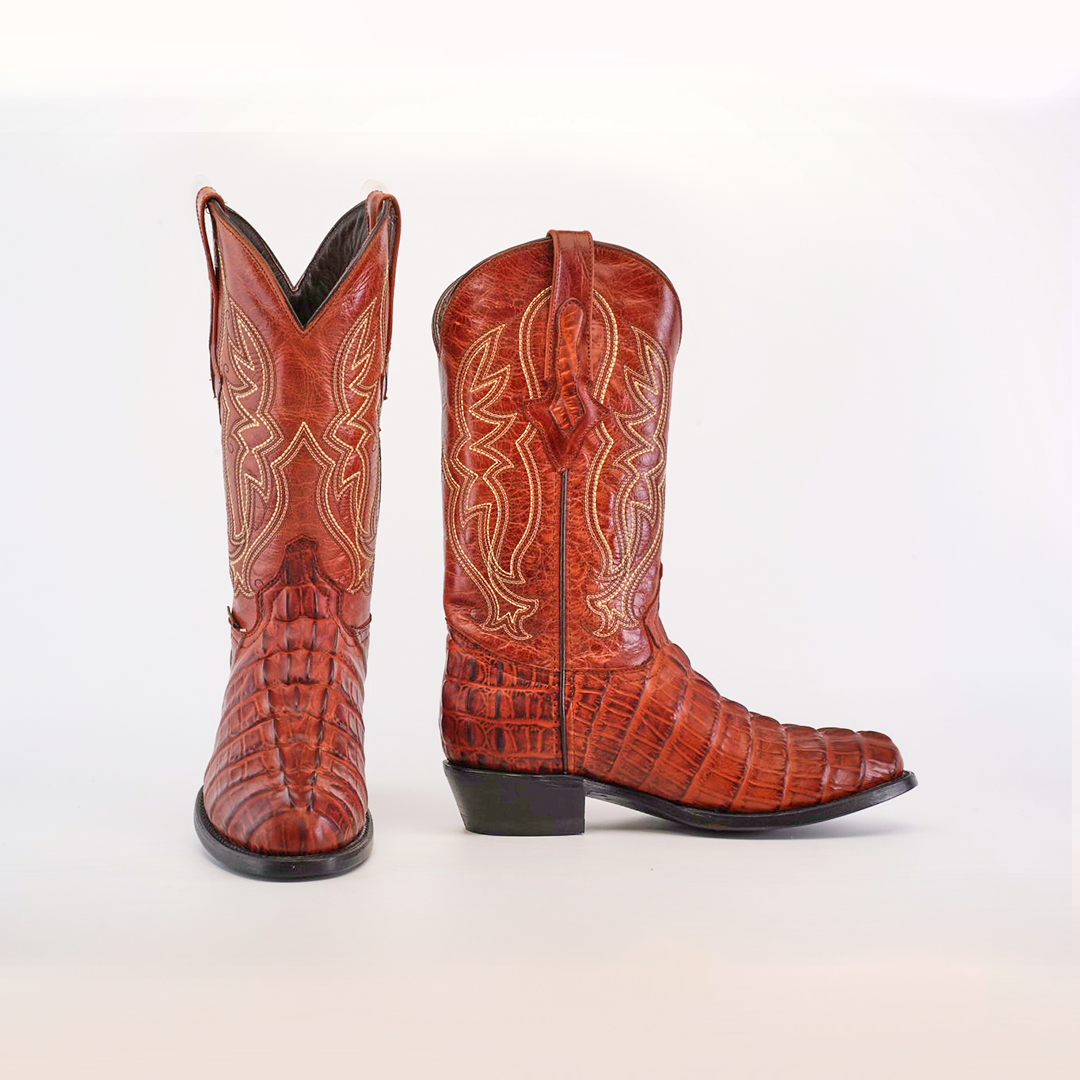 The Crocodile Tail Print Cogñac - Round Toe cowboy boots, crafted from reddish-brown cowhide leather with intricate stitching, feature one boot angled to show the side and the other facing forward to highlight the premium leather sole and design, set against a plain white background.