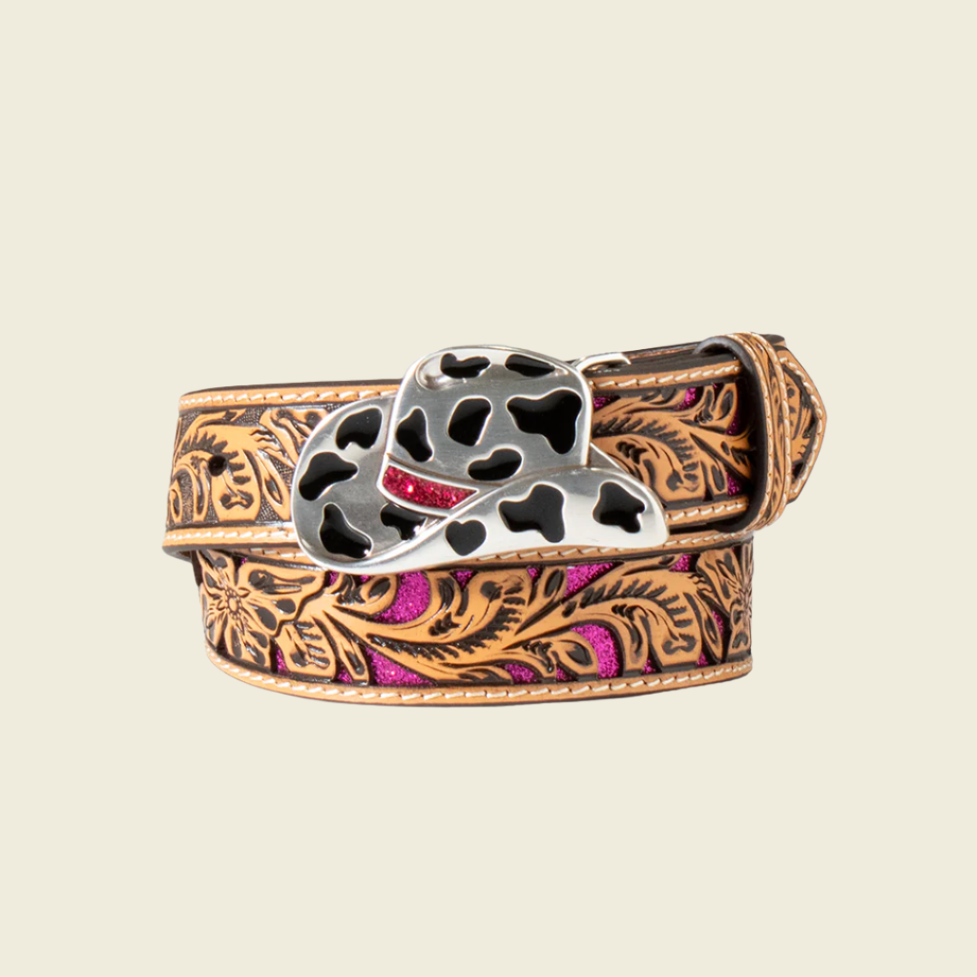 The Angel Ranch Western Girl Belt, model D130003648, is a coiled cowboy-style belt with intricate brown floral engravings and pink accents. It features a metal buckle shaped like a cowboy hat with black cow print patterns, set against a light beige background for Western-inspired flair.