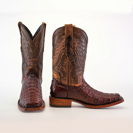 A pair of Exotic Caiman Hornback cowboy boots in brown with intricate stitching is displayed on a white background. The left boot shows the rodeo toe, while the right boot reveals a side view, emphasizing the detailed leather texture and design.