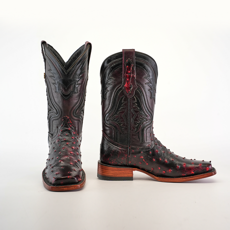 Exotic Ostrich - Black Cherry boots: A pair of authentic ostrich leather cowboy boots in black adorned with red accents and intricate stitching. They feature a rodeo toe and a wooden heel, set against a white background.