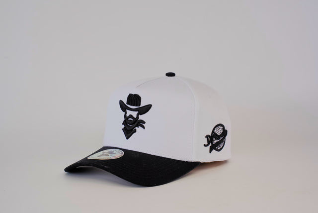 The De Rancho Cap Black & White showcases a cowboy logo embroidery on the front, celebrating Western heritage. It features a small round side logo, a white front panel, and a black brim, all set against a plain white background.