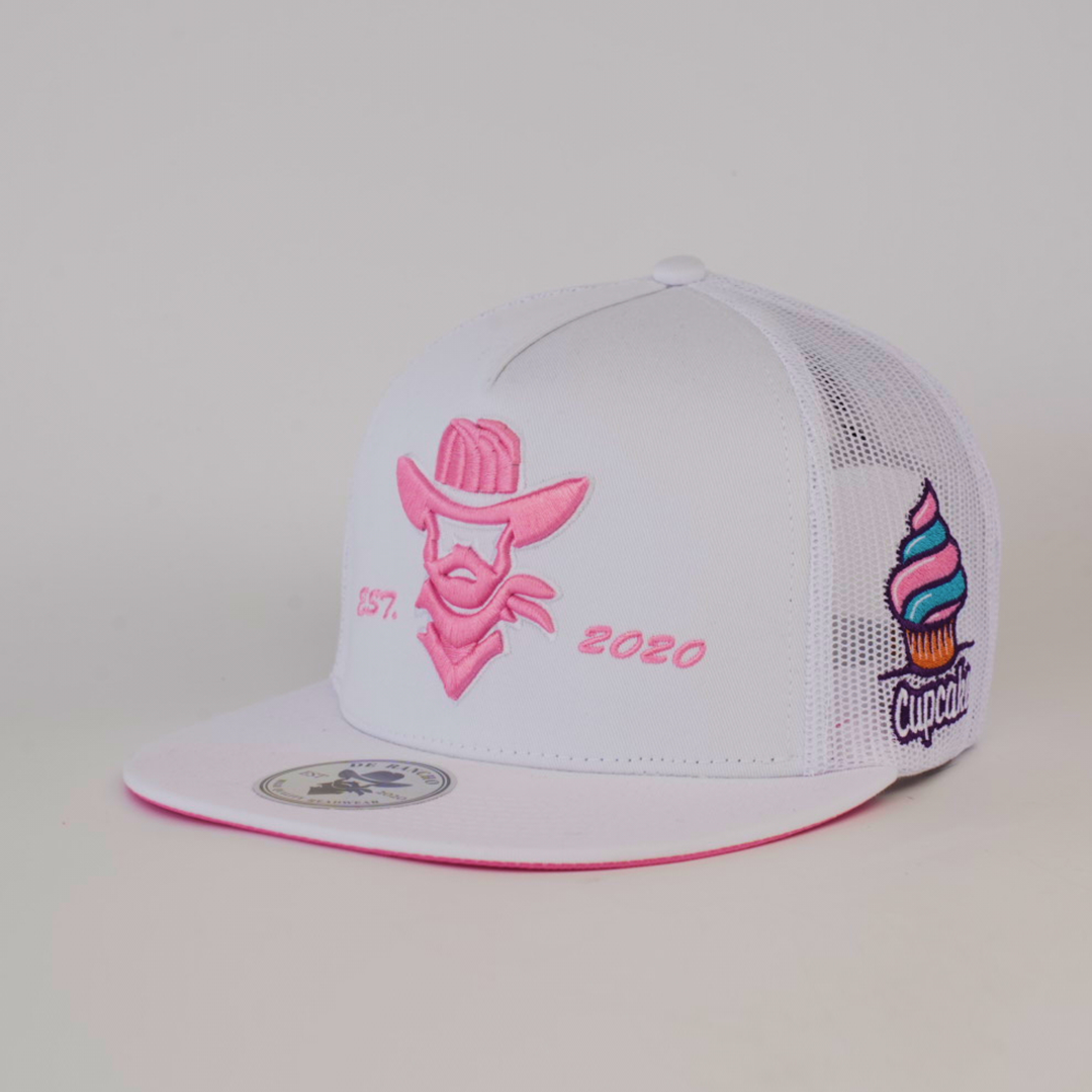 The De Rancho Cap Cupcake White features a white design with pink embroidery, showcasing a cowboy silhouette and EST. 2020 text. A cupcake graphic on the side reads Cupcake. It has embroidered designs, mesh back, and flat brim, celebrating Western heritage.