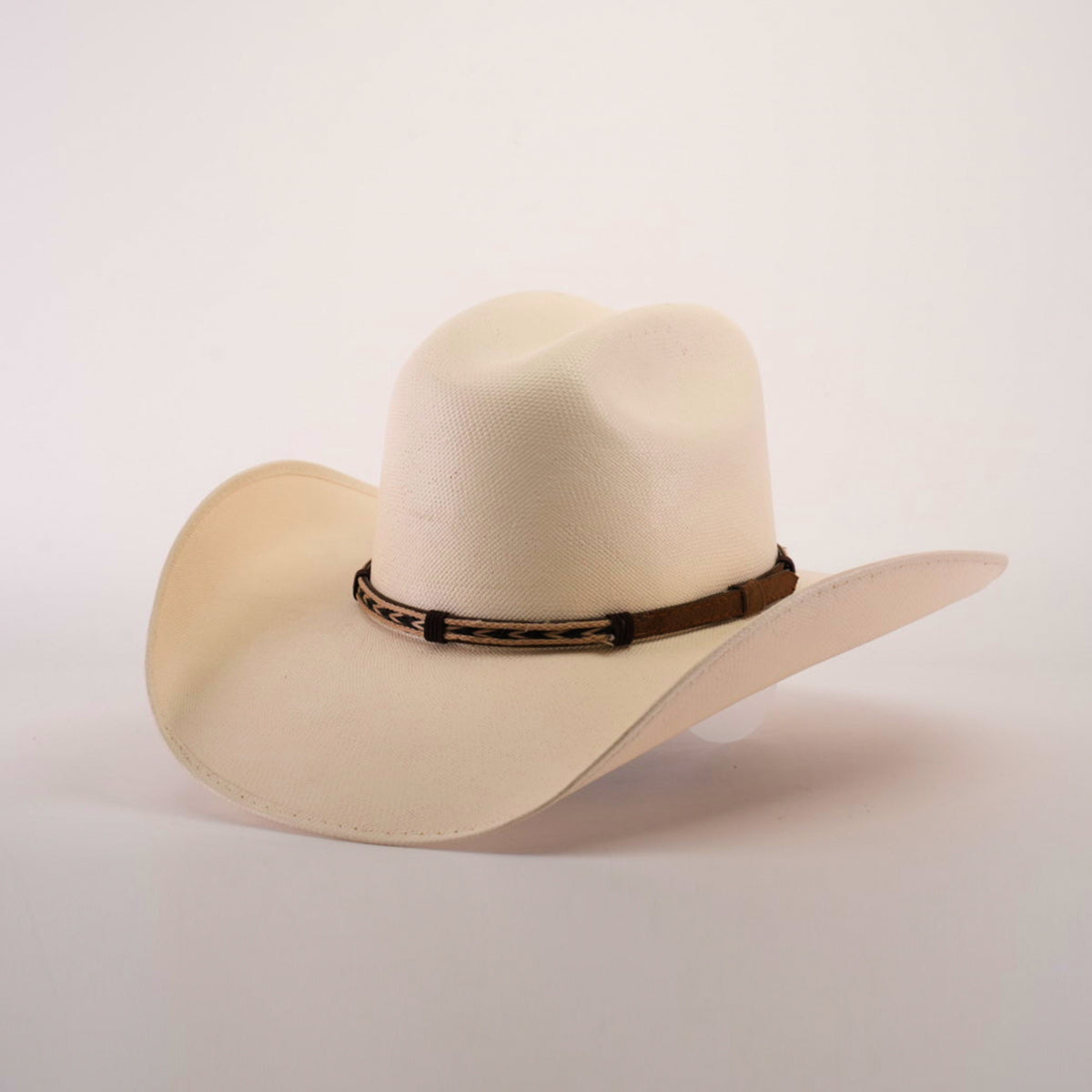 The 5000x Chihuahua Straw Hat, featuring a cream color, wide brim, and brown band, showcases exquisite craftsmanship as it sits angled on a white surface.