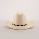 The 1000X Dos Carnales Straw Hat is a white cowboy hat with a wide brim and a black band adorned with silver conchos, crafted with exceptional quality. It stands out against a light background, proudly showcasing its superior craftsmanship.