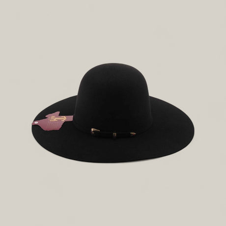 The 4X - Black - TC Hat, featuring a wide brim and shapeable crown, rests on a neutral background. A small maroon tag decorates the brim, while a black band with gold accents encircles the base of the crown.