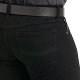 A close-up features someone in the M7 Slim Legacy Straight Jean in Black, showcasing a back pocket, detailed stitching, and a black belt. The modern cowboy vibe exudes rugged charm and pairs beautifully with a dark gray top.