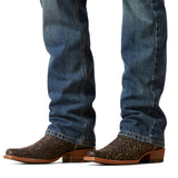 Ariat M7 Slim Ezra Straight Jeans in Brighton style are elegantly tucked into intricately patterned brown cowboy boots, completing the modern cowboy look as the jeans slightly cover the tops. The plain white background enhances this stylish image.