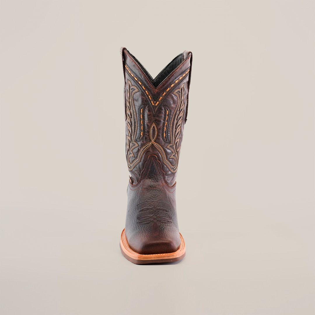 The Cheyenne Chocolate boot, featuring a rodeo toe and intricate stitching, is crafted from premium cowhide for a slightly worn look. Displayed on a white backdrop, it merges style with functionality thanks to its slip-resistant sole.