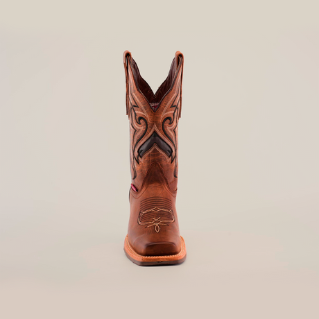 The Fresno Shedron cowboy boot features a single brown cowhide leather design with intricate black and tan stitching on the shaft against a plain white backdrop. It includes a slip-resistant sole, decorative patterns, and a distinctive rodeo toe.