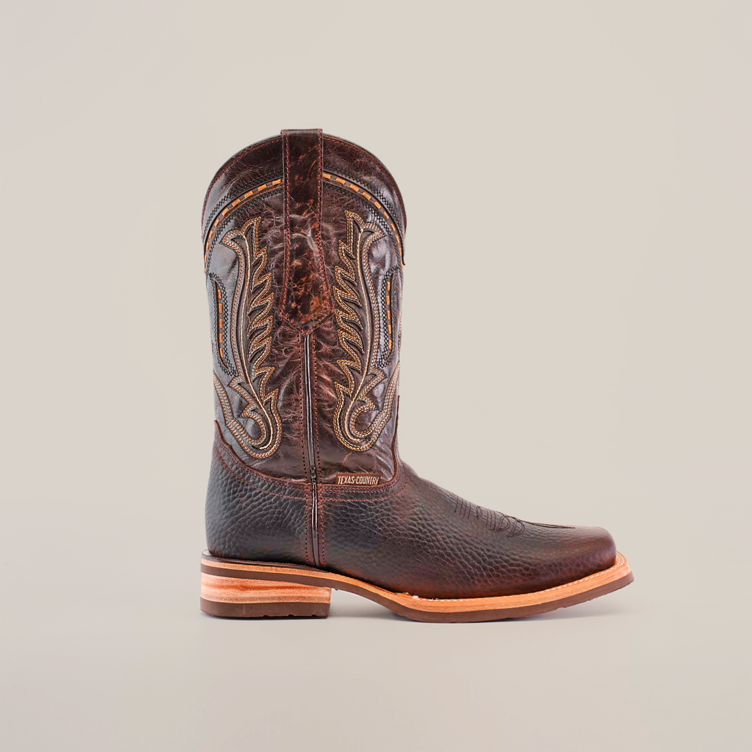 The Cheyenne Chocolate boots feature a brown leather design with intricate embroidery on the shaft, crafted from premium cowhide. They offer a textured surface and functionality with their slip-resistant sole and rodeo toe, all set against a plain white background.