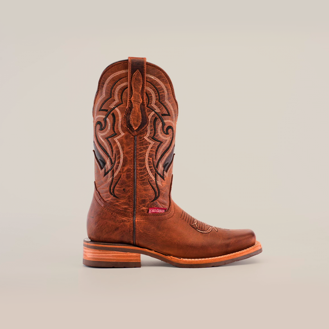 The Fresno Shedron cowboy boot showcases intricate stitching and decorative patterns on cowhide leather. It features a wooden heel, a rodeo toe, and a slip-resistant sole.