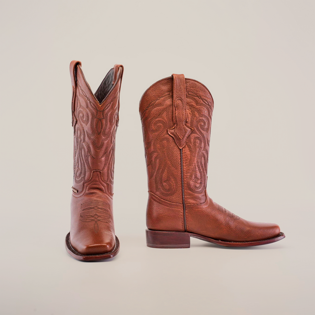 A pair of Grisly Brown - Rodeo Toe cowboy boots stands against a white backdrop. Made from premium cowhide, they showcase intricate stitching and a classic western design with pointed toes and stacked heels.