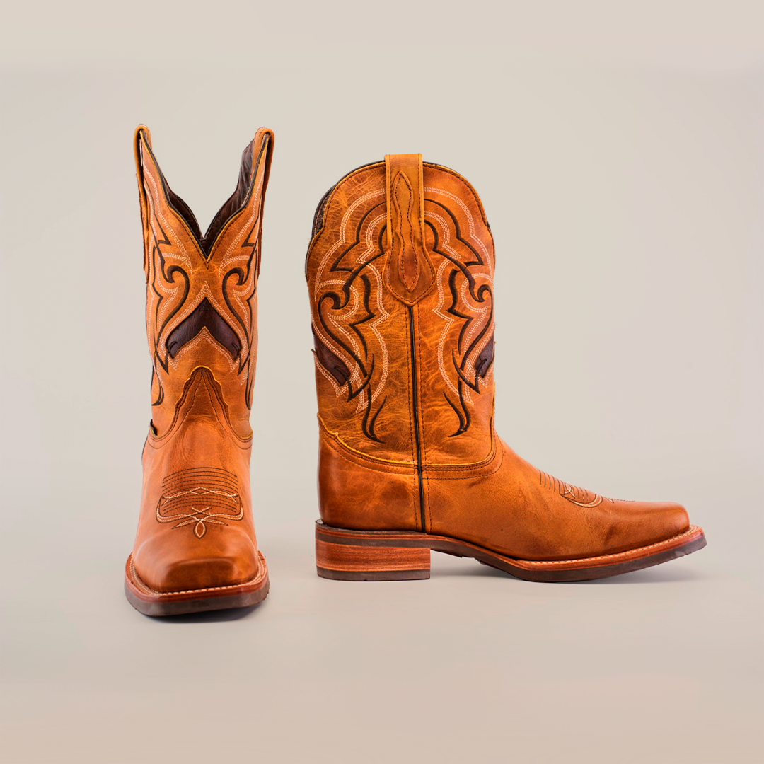 Acrafted from premium cowhide and featuring intricate stitching, is displayed on a plain white background. One stands upright while the other lies on its side, highlighting their wooden heels and slip-resistant soles. pair of Wild Mustard cowboy boots, 