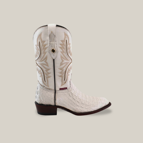 The Exotic Caiman Hornback is a handmade, white round-toe cowboy boot with intricate brown stitching and an embossed texture. Made from authentic Caiman leather, it features a low wooden heel. Displayed in profile on a neutral background, it exudes craftsmanship and style.