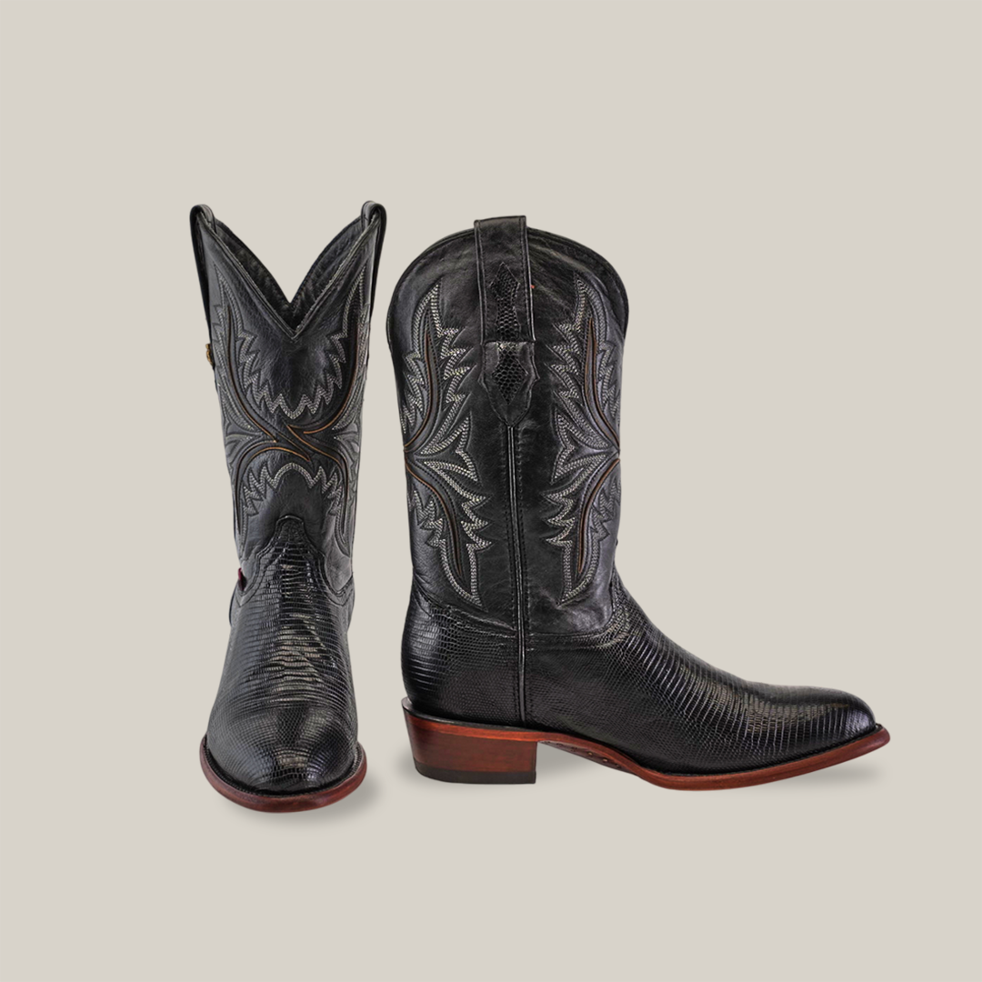 A pair of Exotic Lizard - Black - Round Toe boots features intricate stitching on a light gray backdrop. The left boot leans at an angle, and the right boot stands upright, highlighting their craftsmanship with brown soles crafted from genuine lizard leather.