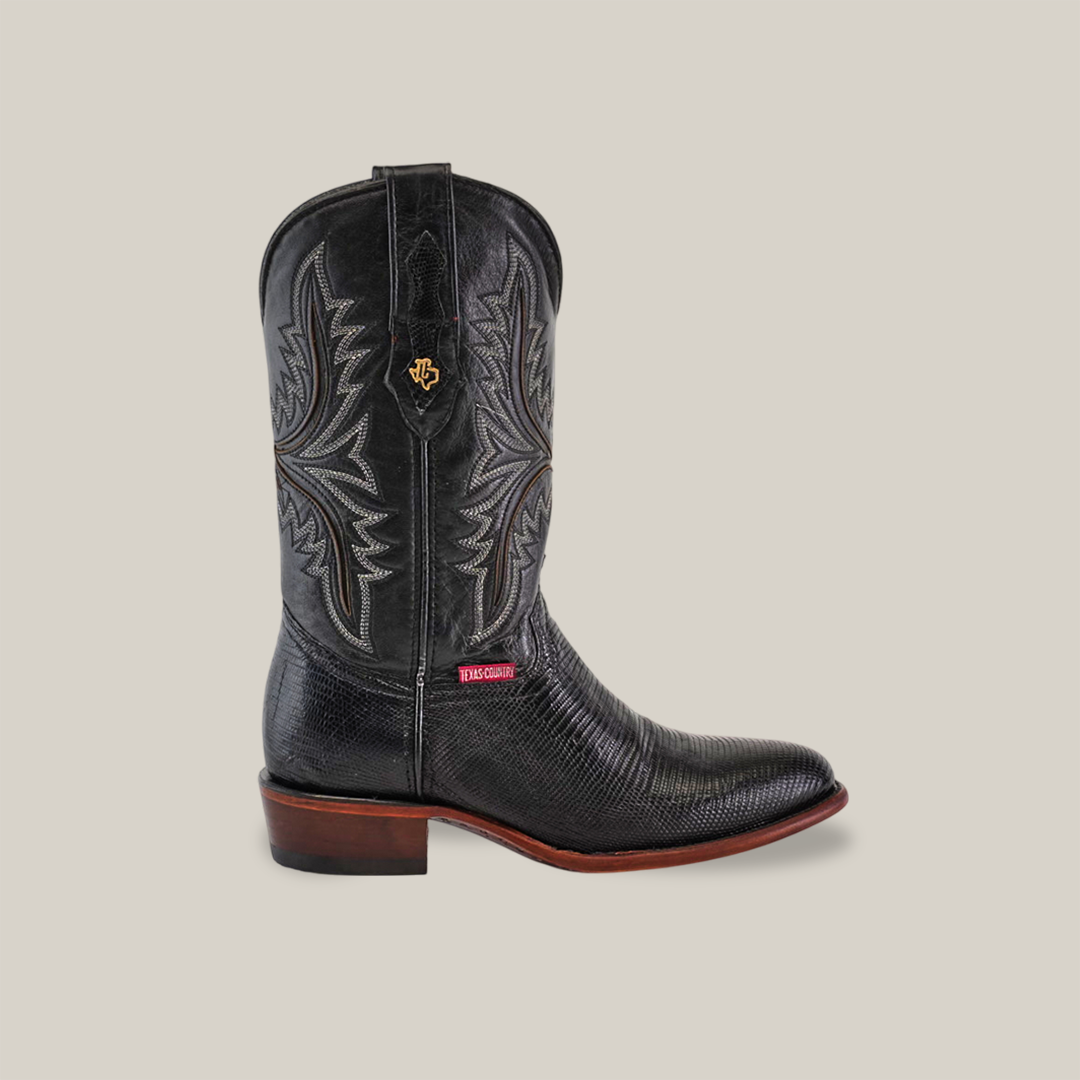 The Exotic Lizard - Black - Round Toe cowboy boot showcases genuine lizard leather with intricate stitching and a decorative emblem on the pull tabs, handcrafted by skilled artisans. It features a dark wooden heel, textured surface, and a red label near the sole on a plain background.