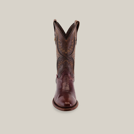 A forward-facing exotic lizard skin cowboy boot in brown, featuring intricate stitched patterns on the shaft and a round toe, is displayed on a light background, showcasing its craftsmanship.