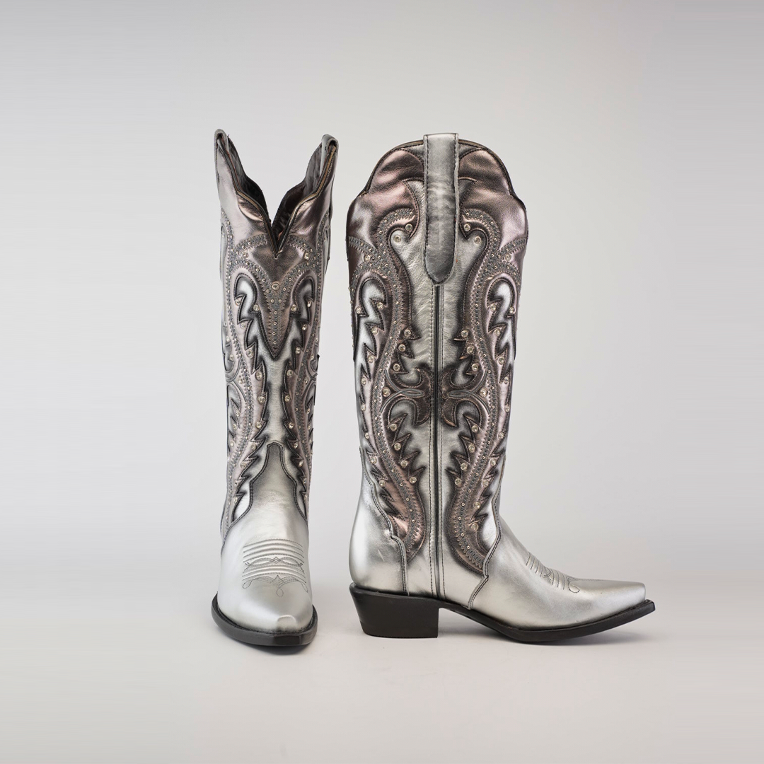 A pair of handcrafted Valentina Silver - Tall Shaft - Snip Toe cowboy boots in metallic silver and bronze, featuring intricate swirling patterns. One boot stands upright, the other angled to highlight the pointed toe and low heel against a light gray background.