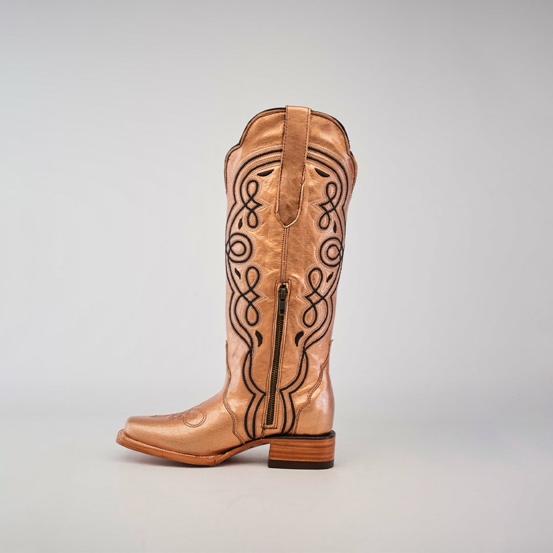 A single Eden Rose Gold boot, with tan leather and intricate black embroidery, stands elegantly against a light gray background. It features a narrow square toe, side zipper, and wooden heel, adding an elegant touch to its design.