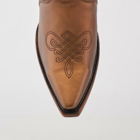 A close-up of a brown leather cowboy boot, similar to Nihan Copper - Tall Shaft - Snip Toe, displays intricate embroidered swirls. The handcrafted quality is evident in the pointed snip toe and dark stitching along the edges against a plain backdrop.