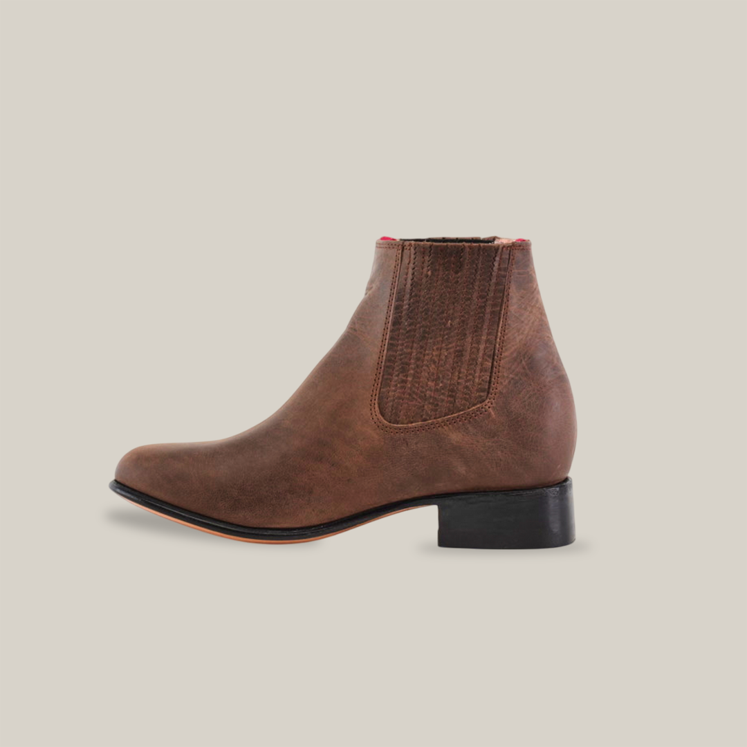 The Alamo Brown - Round Toe ankle boot features premium leather with a sleek, slightly rounded toe and a black low heel. An elastic side panel ensures easy wear, all highlighted against a white background to emphasize its minimalist elegance.