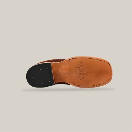 The image displays the underside of the Cowhide Hair Camel Square Toe, a classic Western shoe with a brown leather upper and wooden sole. It features a black textured rubber insert on the heel, metal rivets, embossed brand details on the arch, and is completed with a sleek square toe design.