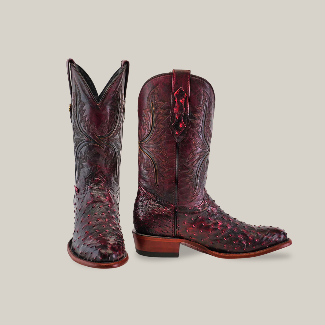 A pair of handcrafted Exotic Full Quilt Ostrich boots in rich Black Cherry, featuring intricate patterns. One boot stands upright and the other leans slightly, showcasing both side and top design details.